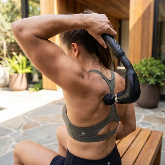 Femme sportive utilisant le masseur à percussion manche long sur l'omoplate après l'entraînement