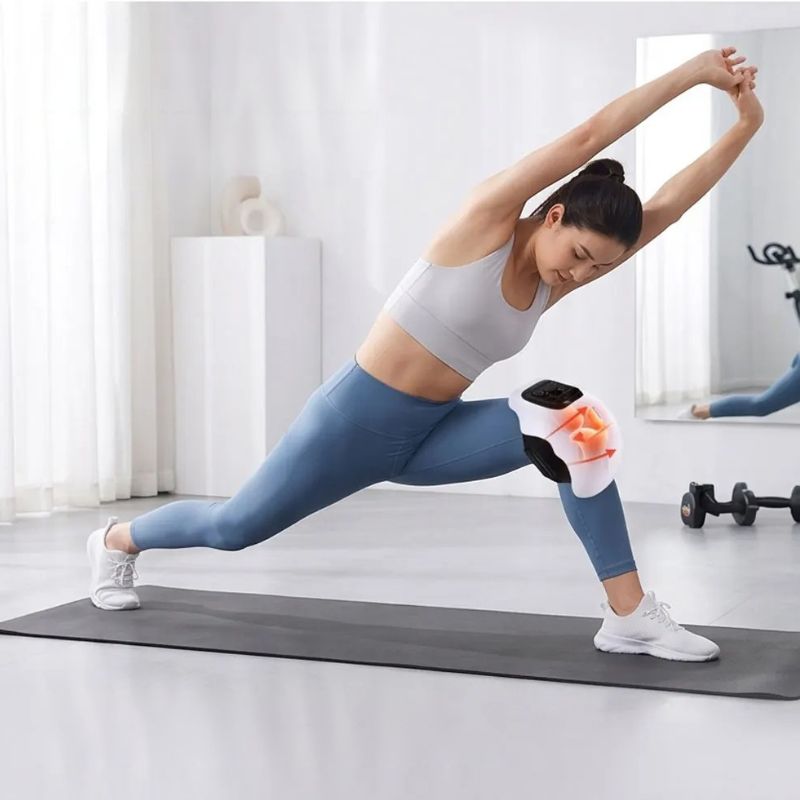 Femme en étirement de yoga avec le masseur de genou électrique chauffant en action
