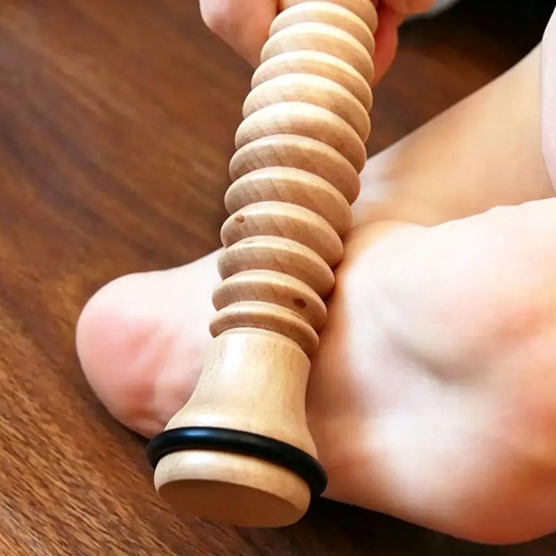 Gros plan du rouleau masseur en bois massif texturé en appui sous la voûte plantaire, fond bois