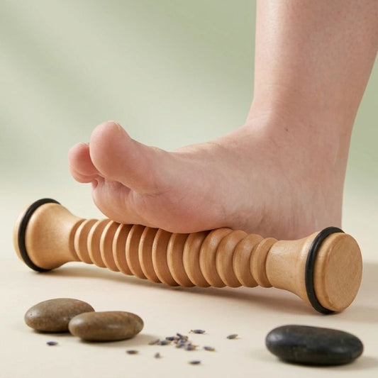 Rouleau masseur pieds en bois massif posé sous un pied nu, ambiance spa avec galets et lavande